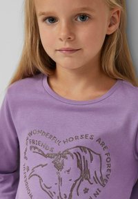 Lavendel langarm shirt met een ronde halslijn. Heeft een glinsterende paardafbeelding en tekst in een cirkelvormige lay-out. Zachte stofstructuur.