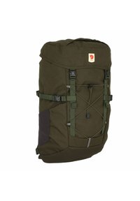 Dark green backpack with a soft fabric texture, adjustable straps, and a roll-top closure. Features a logo patch and elastic cord for extra storage.