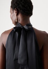 Čierny halterneck top s veľkou mašľou na výstrihu, vyrobený z hladkej látky, s jemným leskom a elegantným, priliehavým strihom.
