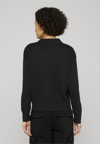 Čierny pletený sveter s rebrovaným spodným lemom a manžetami, so klasickým golierom a uvoľneným strihom. Viditeľné švy na chrbte pre textúru.