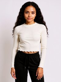 Ribbed cream long-sleeve top with a cropped hem and raw edge detailing, paired with black drawstring pants.