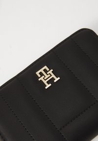 Black leather wallet with quilted texture, featuring a gold logo accent. Smooth finish with visible stitching details on edges.