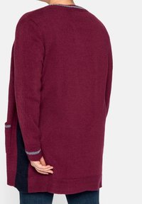Cardigan lungo bordeaux con una finitura testurizzata, dotato di tasche laterali, un accento grigio sul collo e un design aperto sulla schiena.
