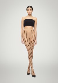 Collant beige con motivo a grandi pois neri. Texture liscia, design a vita alta. Indossati con un top nero senza spalline e tacchi a punta.