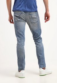 Ljusblå denimjeans med en figurnära design, med två bakfickor och bleknade detaljer. Bärs med vita sneakers och en blå skjorta.