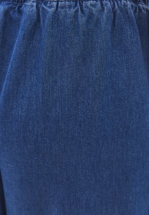 Gros plan sur un tissu en denim bleu foncé avec un détail de ceinture élastique froncée.