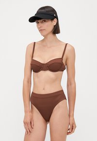 Rjav rebrast bikini zgornji del z obročem; ujemajoči se visokotlačni bikini spodnji del. Obe kosu sta izdelani iz strukturirane tkanine. Črna vizirka kot dodatek.