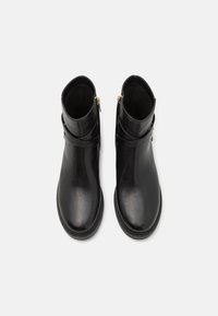 Černé kožené kotníkové boty s hladkou texturou, kulatou špičkou a bočními zipy. Obsahují dekorativní pásek a gumovou podrážku.