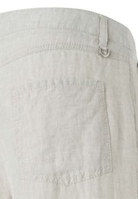 Primo piano di una tasca di pantaloni in lino beige chiaro con cuciture visibili e un piccolo D-ring in argento attaccato a un passante della cintura.