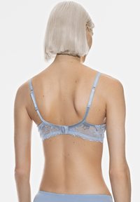 Vaaleansininen pitsiliivi, jossa on satiininen vyö ja säädettävät olkaimet, koristeena haukkasilmukat ja takana hakaskiinnitys.