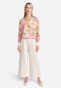 Long-sleeve floral top featuring pink, yellow, and green designs; paired with cream wide-leg pants and pointed flat shoes.