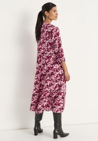 Maxi-jurk in een roze en paarse bloemenprint, gelaagd ontwerp, lange mouwen, lichtgewicht stof. Gepaarde met kniehoge zwarte laarzen.