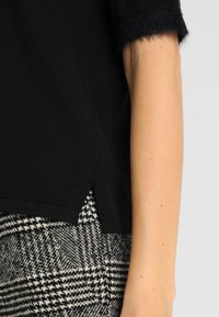Top negro de manga corta con puños de felpa, con una abertura lateral. Combinado con un tejido de pata de gallo en blanco y negro.