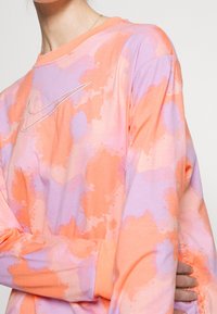 Lätt långärmad skjorta i bomull med ett tie-dye-mönster i orange och lavendel samt en liten Nike-logotyp i silverfärg på bröstet.