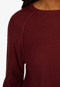 Bordeauxfarbener Strickpullover mit strukturiertem Muster, Rundhalsausschnitt und Raglanärmel, aus weichem, atmungsaktivem Material gefertigt.