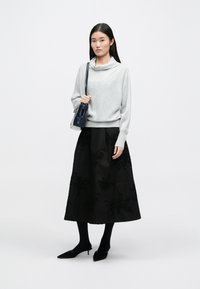 Γκρι πουλόβερ με κολάρο, συνδυασμένο με μια μαύρη φούστα με λουλουδάτα κεντήματα. Το μοντέλο κρατά μια μικρή ναυτική τσάντα, φορώντας μαύρες καλσόν και μυτερές γόβες.