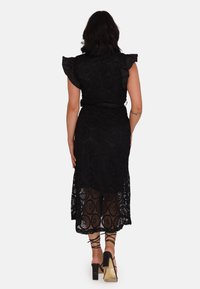 Abito in pizzo nero con corpetto aderente, maniche a ruffled e gonna di lunghezza media con motivo floreale. Indossato con sandali con tacco largo.