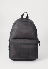 Zaino nero con texture, dotato di una tasca anteriore con zip, manico superiore e logo "HUGO" impresso sulla tasca, su sfondo bianco.