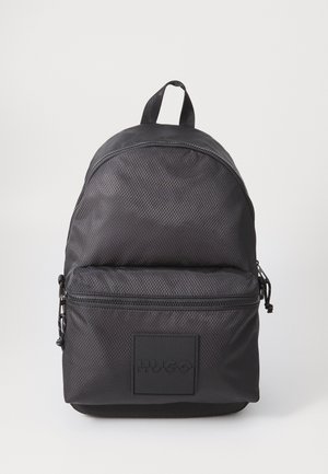 Mochila preta texturizada com um bolso frontal com fecho, pega superior e logótipo "HUGO" em relevo no bolso, sobre um fundo branco.
