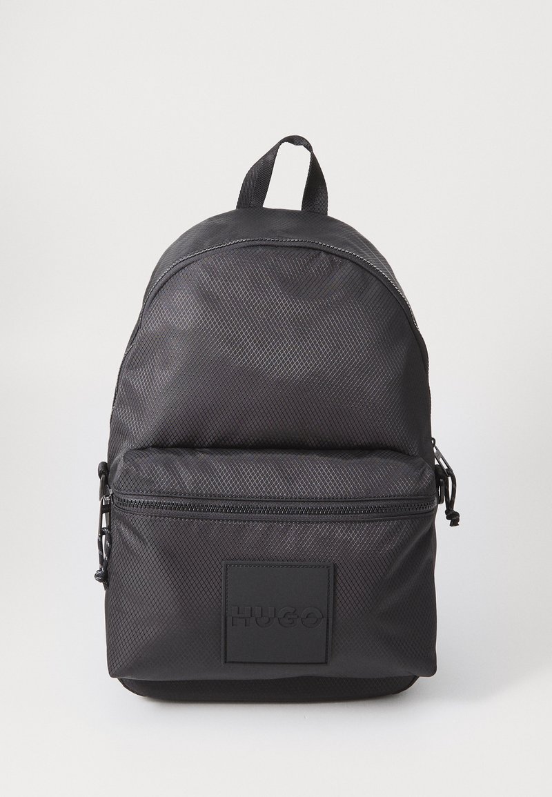 Zaino nero con texture, dotato di una tasca anteriore con zip, manico superiore e logo "HUGO" impresso sulla tasca, su sfondo bianco.