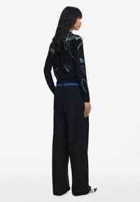 Pull noir avec broderie florale multicolore, associé à un pantalon ample bleu marine avec une ceinture à motif bleu.
