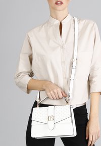 Borsa bianca con un design strutturato, hardware dorato, dettagli borchiati sulla patta e una tracolla rimovibile per un trasporto versatile.