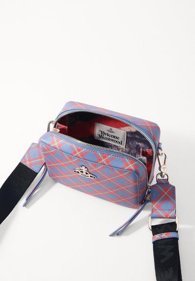 Sac bandoulière à carreaux bleus et rouges, de forme rectangulaire, avec un logo argenté, une fermeture zip et une sangle en tissu avec des accents contrastants.