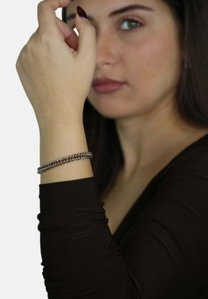 Bracciale in argento con finitura liscia, indossato su un polso leggermente abbronzato, con una maglietta nera a maniche lunghe visibile.