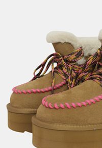 Stivali scamosciati color panna con un collo in shearling bianco, lacci intrecciati rosa e multicolori, e una suola in gomma spessa. Dettagli cuciti a mano.