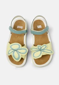 Sandali per bambini con una base gialla, design a fiore blu, suole interne marroni e una fascia regolabile azzurro chiaro.