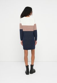 Abito lavorato a maglia con blocchi di colore verticali: crema, malva e blu navy. Maniche lunghe, scollo rotondo e forma aderente. Texture liscia.