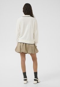 Lightweight cream sweater with a collar, paired with a pleated beige skirt. Features black trim on the sweater and chunky white heeled shoes.
