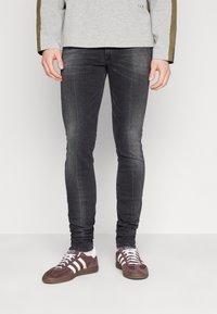 Jeans ajustados gris con un ligero desgaste, combinados con zapatillas de ante burdeos con rayas blancas. Apariencia casual con detalles mínimos.