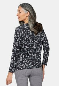 Langarmige zwarte shirt met witte en grijze abstracte patronen. Zachte stof, gebogen zoom en een relaxte pasvorm, gecombineerd met grijze broek.