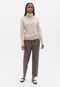 Jersey de cuello alto beige con mangas largas, combinado con pantalones de cuadros marrones y zapatos en blanco y negro. Diseño minimalista y textura suave.