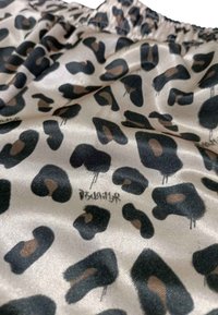 Tessuto leopardato con motivi neri e marroni su uno sfondo beige chiaro, caratterizzato da una superficie liscia e dettagli con cintura elastica.