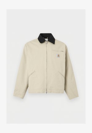 Veste Carhartt beige avec col noir, fermeture éclair frontale complète, deux poches latérales et une petite poche poitrine zippée avec écusson logo.