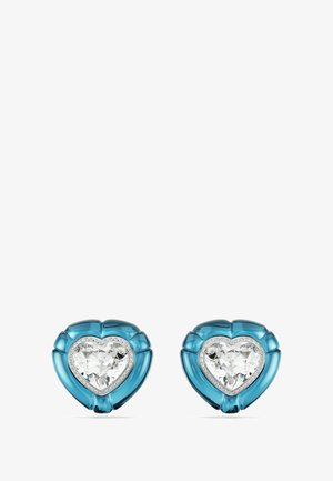 Boucles d'oreilles en forme de cœur en matériau translucide turquoise avec une pierre centrale claire et facettée, accentuée d'un cache en métal argenté.