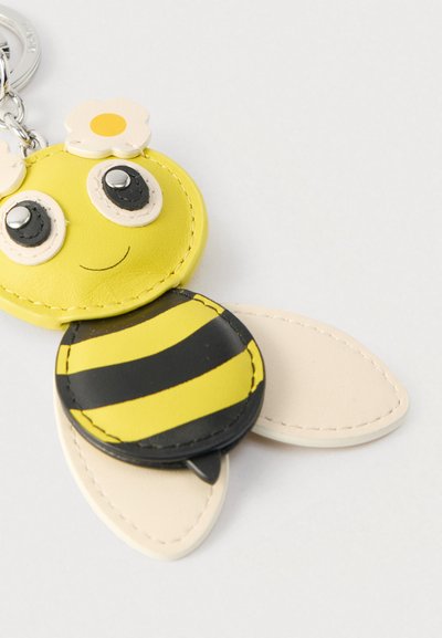 Κίτρινο μπρελόκ μέλισσας από δέρμα με μαύρες ρίγες και λευκά ανθισμένα στοιχεία. Στρογγυλό κεφάλι και επίπεδα φτερά, με εμφανείς ραφές.