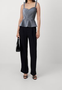 Top peplum con un patrón de cuadros en blanco y negro, escote corazón, correas ajustables; combinado con pantalones de pierna ancha negros y zapatos de tiras.