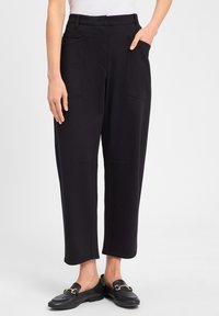 Zwarte, cropped broeken van zacht materiaal met twee voorzakken en een getailleerde pasvorm. Gecombineerd met zwarte loafers met een gouden accent.