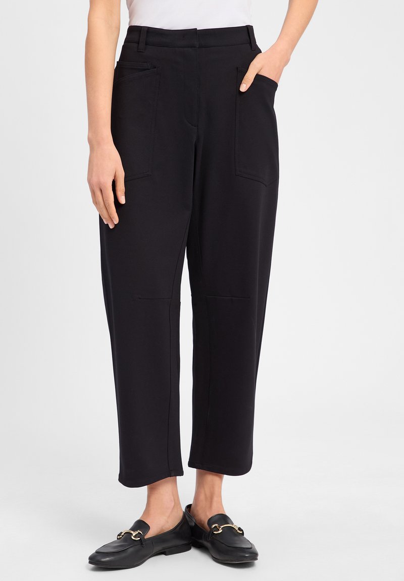 Zwarte, cropped broeken van zacht materiaal met twee voorzakken en een getailleerde pasvorm. Gecombineerd met zwarte loafers met een gouden accent.