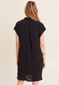 Abito nero a maniche corte con colletto, caratterizzato da una vestibilità rilassata e un sottile dettaglio di piega sul retro. Tessuto morbido e leggero.