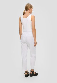 Weißes Trägershirt und leichte, locker sitzende weiße Hose mit elastischem Bund. Schwarze Sandalen mit Riemchen vervollständigen das Outfit.