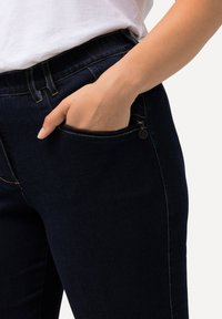 Jeans de mezclilla azul oscuro con una textura suave, que cuentan con un bolsillo lateral con cremallera y costuras en contraste a lo largo de las costuras.