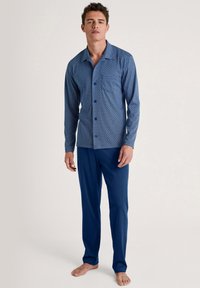 Navyblauwe pyjama set met een patroon, bestaande uit een knoop-over lange mouwen overhemd met geometrische ontwerpen en bijpassende effen blauwe broek.