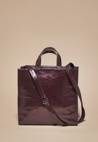 Bolso tote de cuero burdeos con acabado brillante, que cuenta con asas cortas y una correa de hombro ajustable. Forma cuadrada con detalles mínimos.