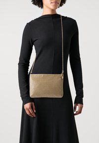 Zlatá síťovaná taška přes rameno obdélníkového tvaru s texturovaným povrchem a řetízkovým popruhem. Obsahuje malý zip a kovové ozdoby.