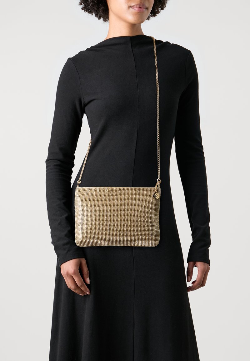 Zlatá síťovaná taška přes rameno obdélníkového tvaru s texturovaným povrchem a řetízkovým popruhem. Obsahuje malý zip a kovové ozdoby.