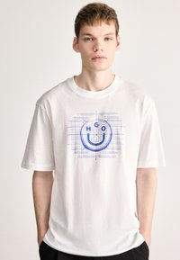 Camiseta blanca de algodón con un diseño gráfico azul que incluye una cara sonriente y las letras "HGO" sobre un fondo de cuadricula. Manga corta, corte relajado.